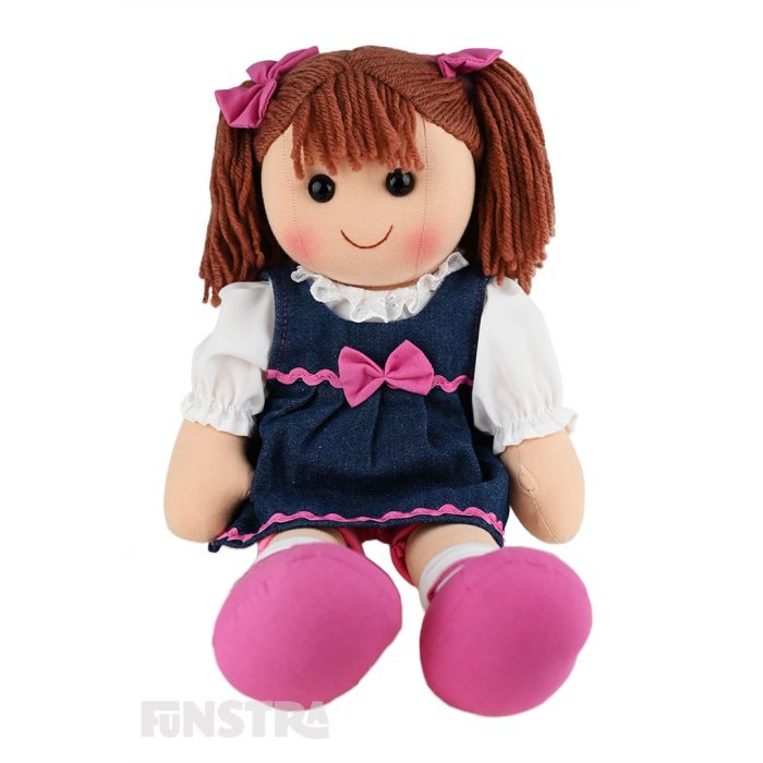 Lacey is a funky doll with a soft cloth body and brown hair tied in pigtails with pink bows and wears a denim dress embellished with pink ribbon and a bow over a white shirt and pink bike shorts.