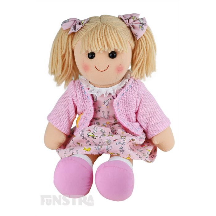 Willow is an adorable doll with a soft cloth body and blonde hair tied in pigtails with bows and wears a pastel pink whimsical printed dress and cardigan.